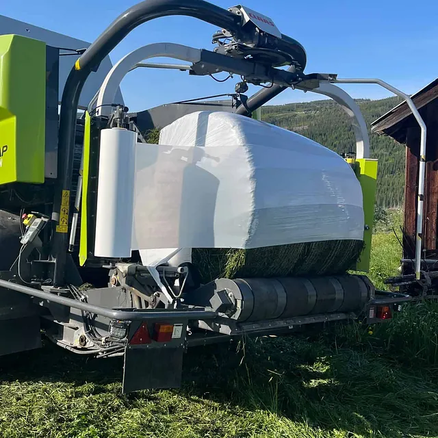 Nærbilde av CLAAS-maskin som pakker rundball med plastfolie.