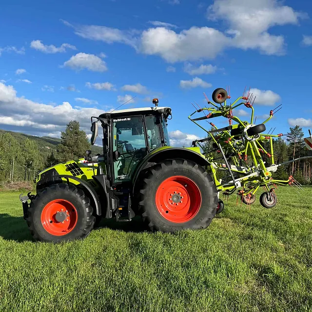 CLAAS-traktor med vendehøyrive parkert på grønt jorde under blå himmel.
