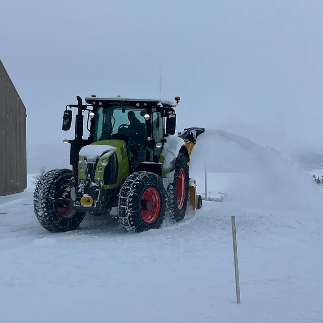 CLAAS-traktor med snøfreser rydder snø utenfor bygning på vinterdag.