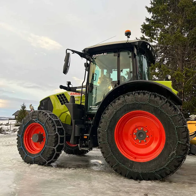 CLAAS-traktor med kjettinger på hjul står parkert på islagt underlag.