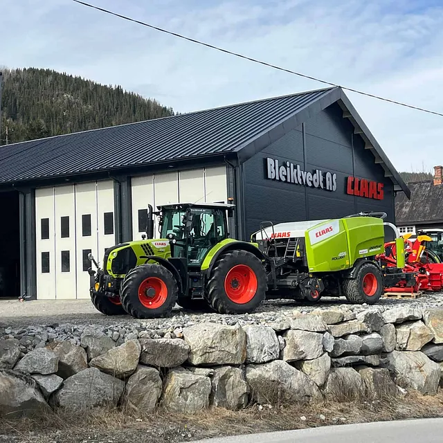 CLAAS-traktor med rundballepresse og annet utstyr foran Bleikvold AS og PALAX-flagg.