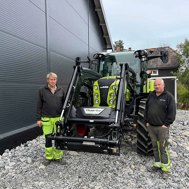 To personer står foran en CLAAS-traktor med frontlaster ved et industribygg.